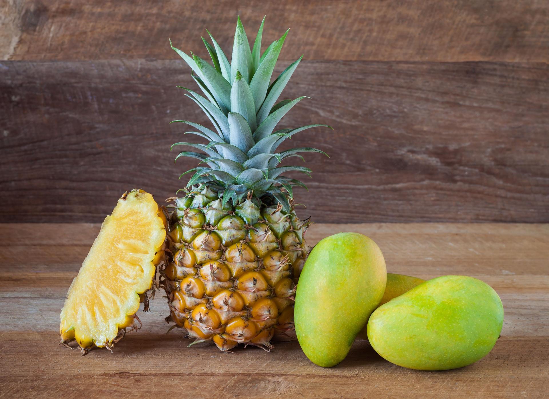 pineapple and mangoes on old wooden background.