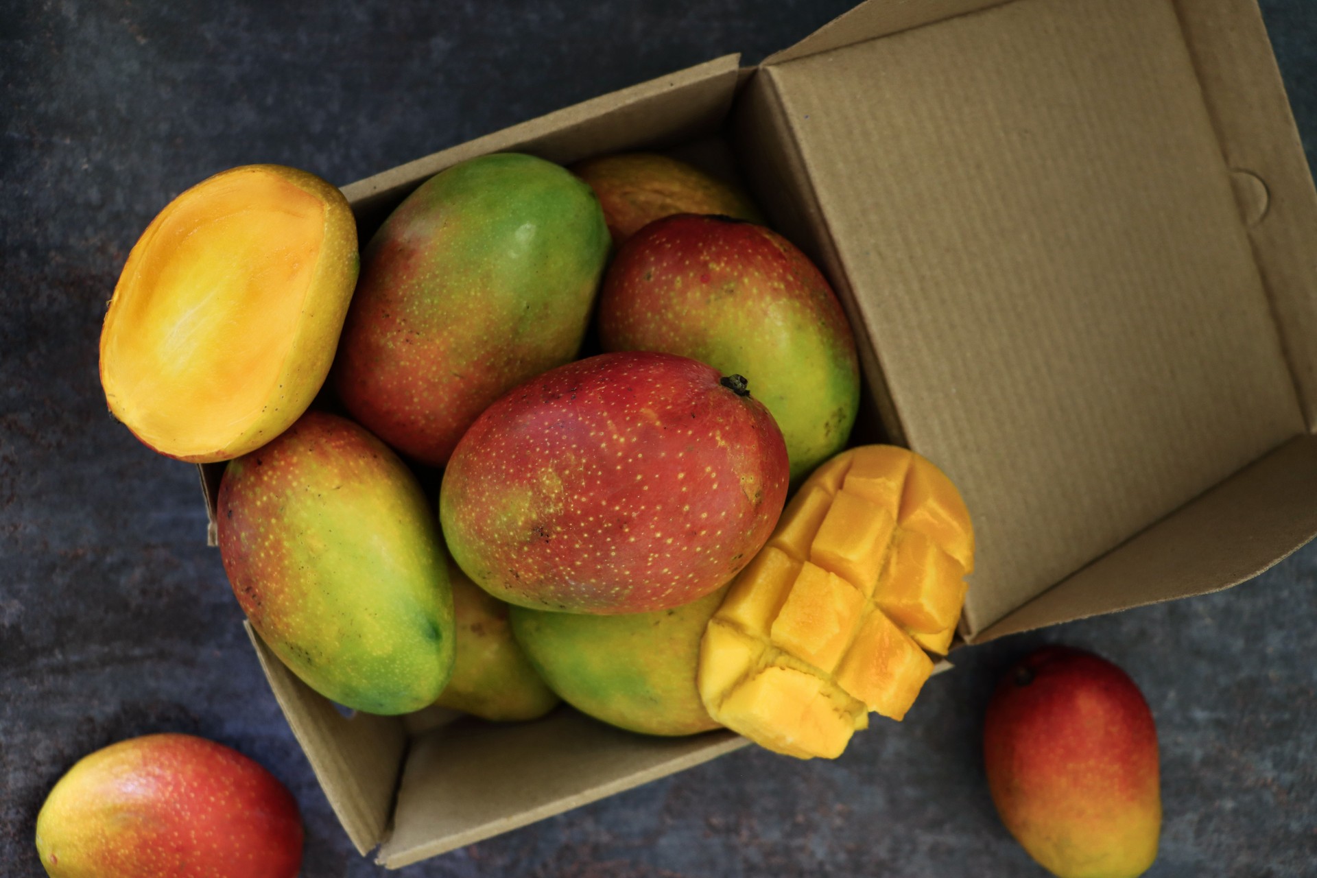 Close-up image of cardboard box full of tropical mango fruit on grey background, elevated view